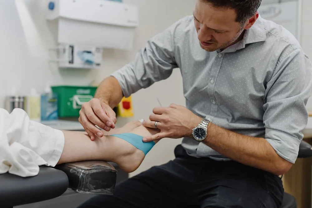 A podiatrist applying supportive strapping tape to a patient in the clinic