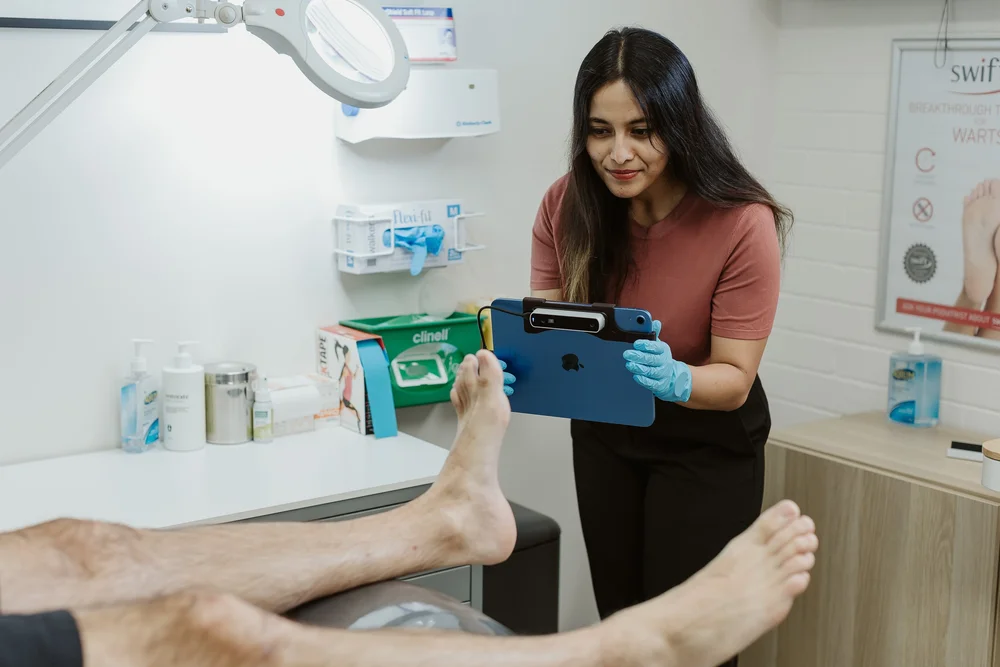 A podiatrist recording assessment notes beside the treatment chair