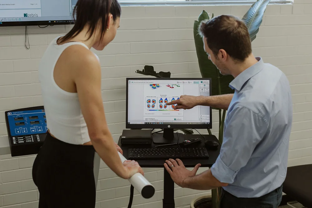 A podiatrist talking a patient through their assessment results on screen
