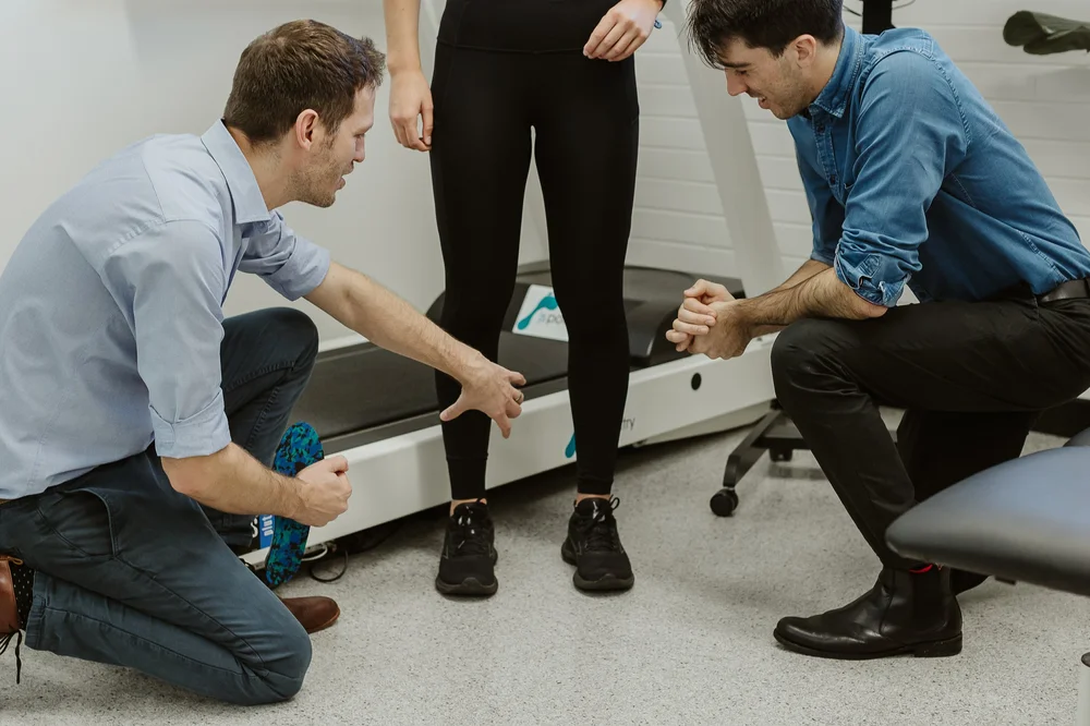 Two podiatrists assessing a patient's feet and legs in standing