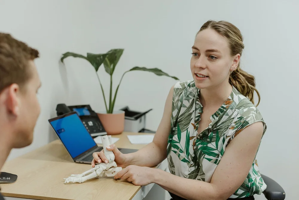 A podiatrist using a model of the foot to explain the bones and joints to a patient